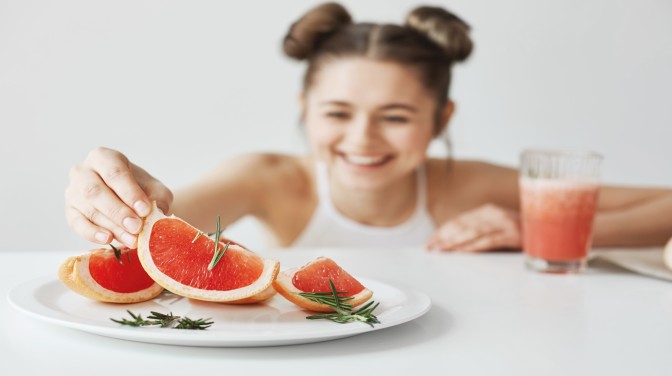 cheerful-woman-smiling-taking-slice-grapefruit-from-plate-sitting-table-white-wall-healthy-fitness-concept-focus-food h_Activ Living Community