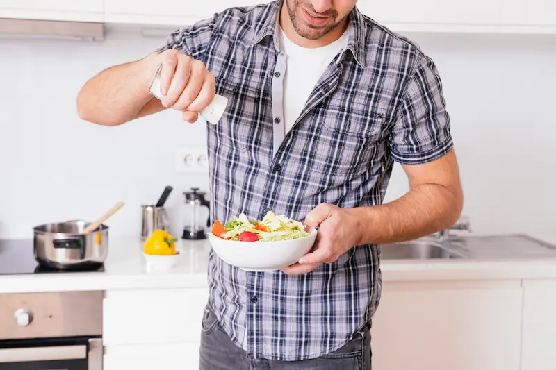 close-up-young-man-adding-salt-vegetable-salad-while-cooking-kitchen_Activ Living Community