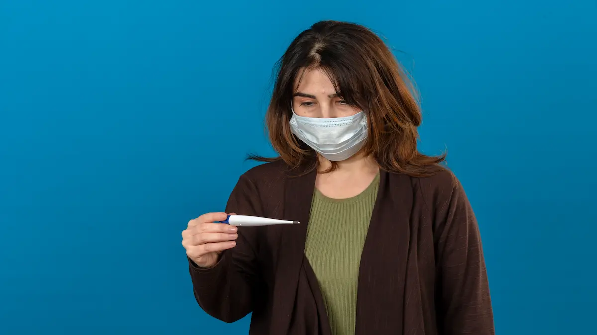 woman-wearing-brown-cardigan-medical-protective-mask-looking-sick-holding-digital-thermometer-looking-it-with-sad-expression-face-isolated-blue-wall_Activ Living Community