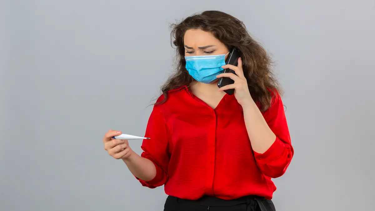 young-worried-woman-wearing-red-blouse-medical-protective-mask-talking-mobile-phone-looking-digital-thermometer-isolated-white-background_Activ Living Community
